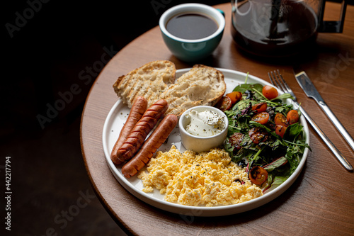 Full english breakfast with scrambled eggs, toast and sausages served with a cup of green tea, dark atmospheric photo