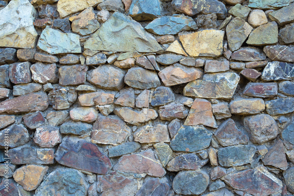 Obraz premium Frontal view of a wall composed of multi-colored brown, gray, brown, black, untreated stones, fastened with cement. .Stones of different shapes. .Texture, background. .