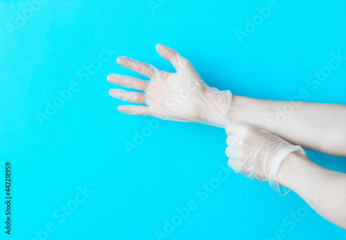 Human hands puting on vinyl disposable gloves above bright blue background with copy space. Safety first concept.