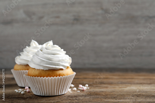 Delicious cupcakes with cream on wooden table. Space for text