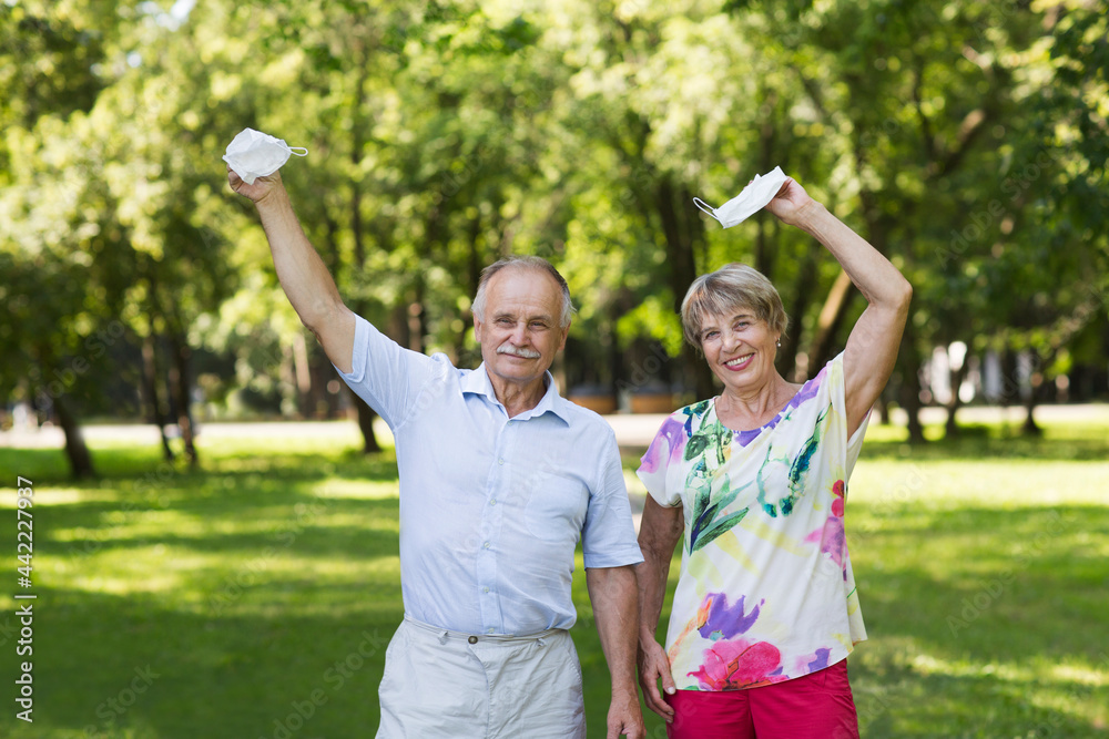 Obraz premium joyful elderly couple hold medical masks with hands up in the summer garden. end of a quarantine. vaccination. lockdown 
