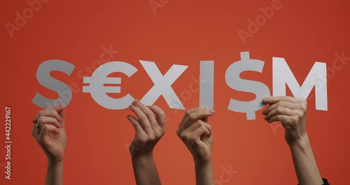 Hands showing word sexism of english language with euro, dollar sign. Word made of carved paper for feminist blog photo