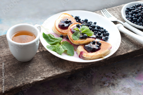 Breakfast with tea  pancakes  fresh blueberries and mint on wooden desk. Fried pancakes on a white plate.