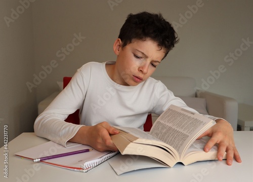 Foto A boy with light skin and brown hair doing homework and looking up a word in the dictionary