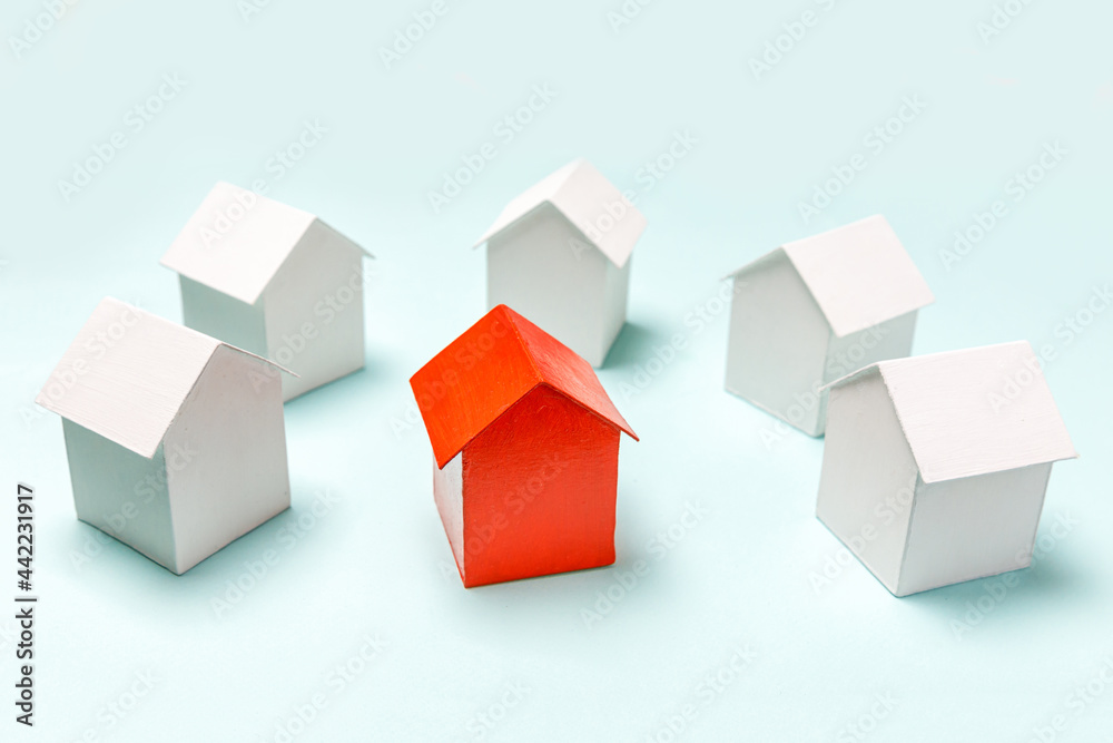 Simply design with miniature red toy model house in among white houses isolated on pastel blue background. Real estate property industry. Community unique neighborhood choice concept. Simply design with miniature red toy model house in among white houses isolated on pastel blue background. Real estate property industry. Community unique neighborhood choice concept.
