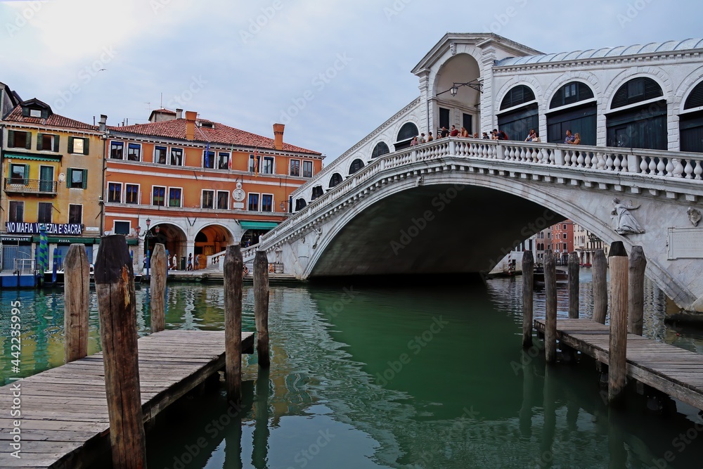 Venice, Italy. June 24, 2020. First tourists on the Rialto bridge after the lockdown for the covid-19 pandemic. In the foreground the empty piers on the grand canal.