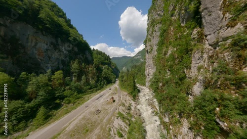 Aerial shot dynamic flying at natural landscape canyon high mountain covered dense green forest and rapid movement river. Shooting from fpv helicopter scenery valley with speed water and asphalt road photo