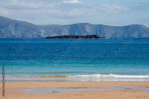 Small stone island in the ocean. Warm sunny day, Blue sky and water. Keem bay, county Mayo, Achill island, Ireland