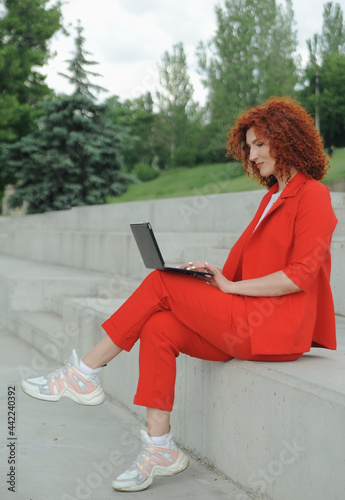 Curly hair business woman in red clothes works ooutdoors. photo