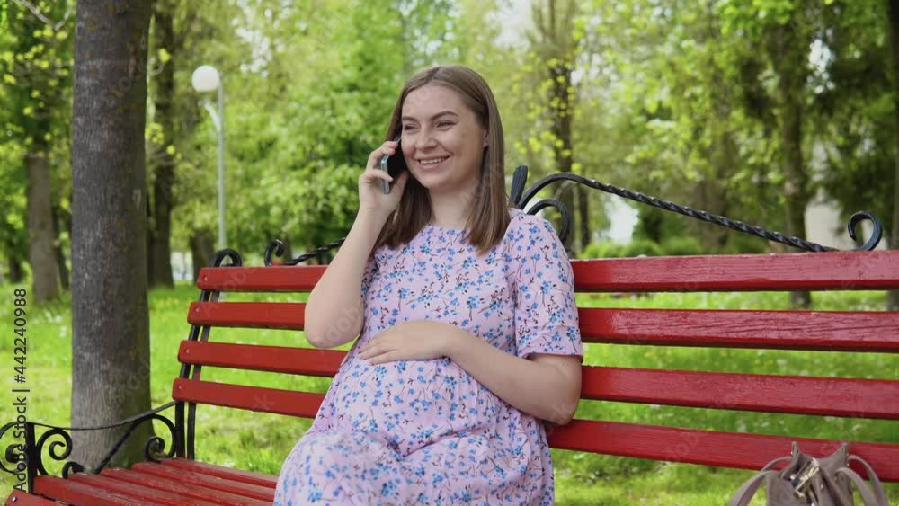 A pregnant woman is sitting in a summer park and talking on a cell phone. Remote consultation with a doctor A pregnant woman is sitting in a summer park and talking on a cell phone. Remote consultation with a doctor