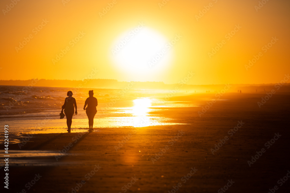Silueta de dos mujeres caminando por la playa al ocaso en vacaciones Silueta de dos mujeres caminando por la playa al ocaso en vacaciones