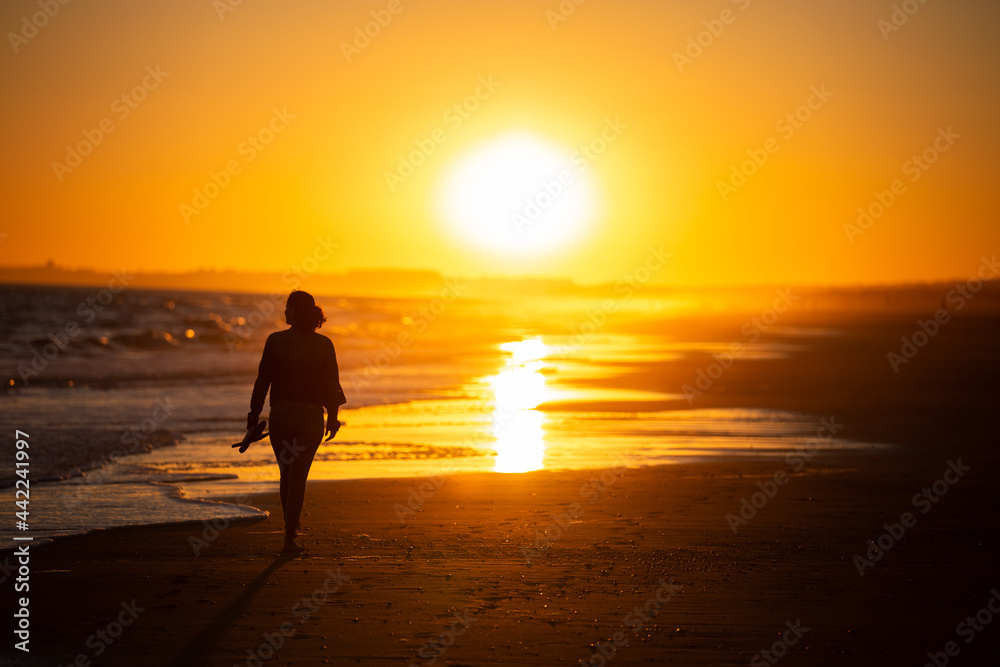 Silueta de mujer caminando al ocaso en la playa en vacaciones