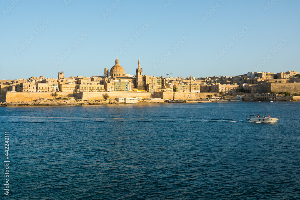 Landscape of Valetta skyline in Malta with boat passing. The stunning skyline of old Valletta, its churches and towers, its historic remparts from the Northern Harbour on golden hour.