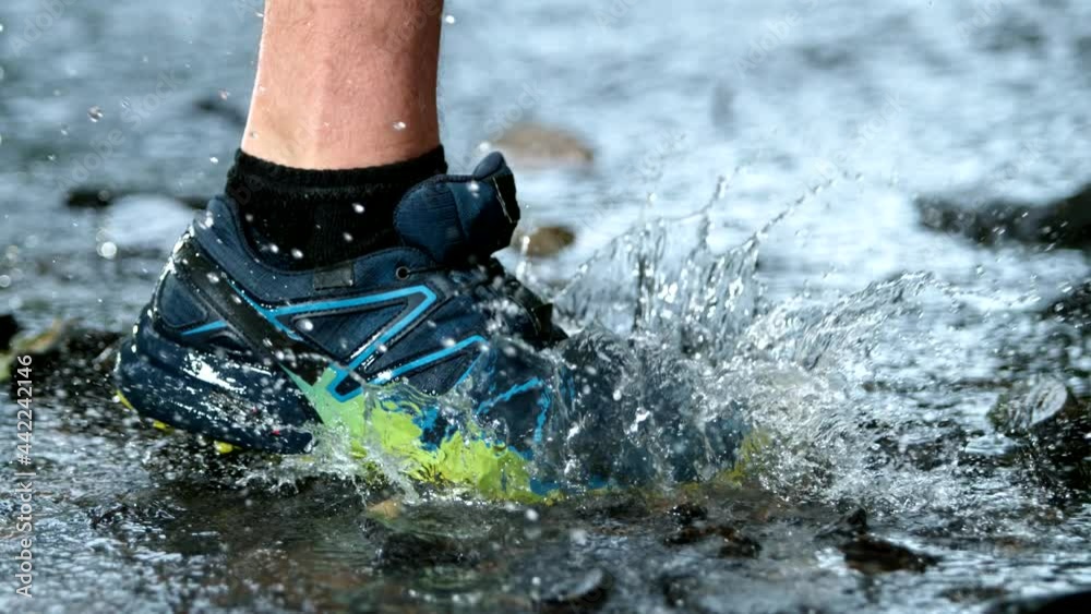 Super slow motion of legs of a runner in sneakers splashng in forest stream. Filmed on high speed cinematic camera at 1000 fps.
