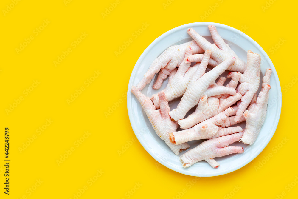 Raw chicken feet in white plate on yellow background. Raw chicken feet in white plate on yellow background.