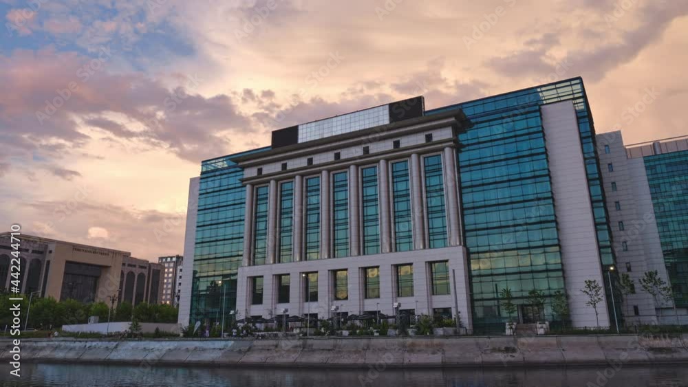 National Library of Romania in Bucharest, public building with reflective glass facade, located in the capital city, at sunset. Timelapse, colorful pink and purple clouds. National Library of Romania in Bucharest, public building with reflective glass facade, located in the capital city, at sunset. Timelapse, colorful pink and purple clouds.