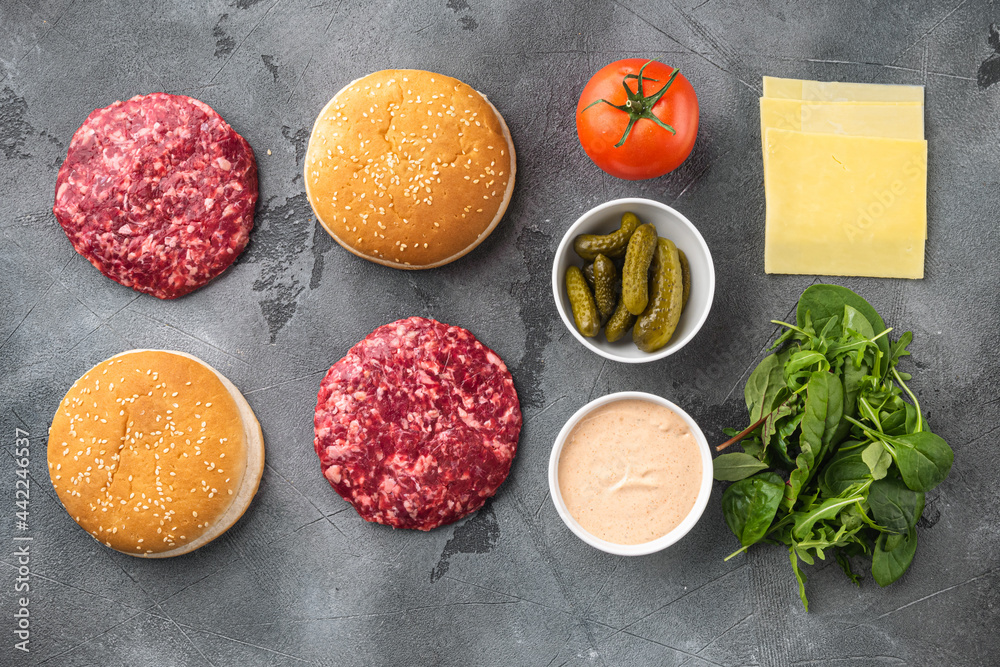 Homemade hamburger. Raw beef patties, sesame buns with other ingredients, on gray stone background, top view flat lay