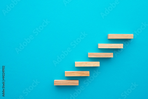 Flat lay of wooden blocks in shape of staircase step on blue background with copy space. Growth or development step by step for successful in business financial or education concept.