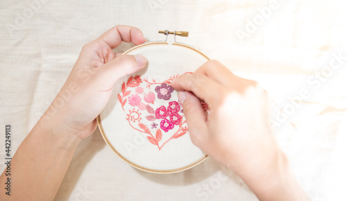 Female hand holding wood embroidery frame and and needle working on flower pattern stitching in a process of handiwork.