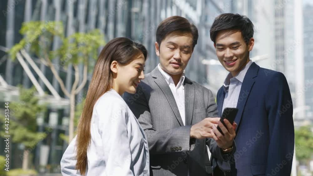 team of asian business people colleagues coworkers having a discussion on city street using mobile phone team of asian business people colleagues coworkers having a discussion on city street using mobile phone