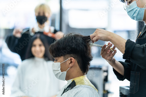 Asian hairdresser barber team wear mask, cut hair of customer in shop. 