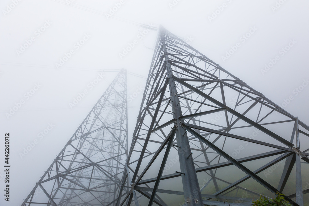 Power line pylons are buried in dense fog. Power lines going to the sky.