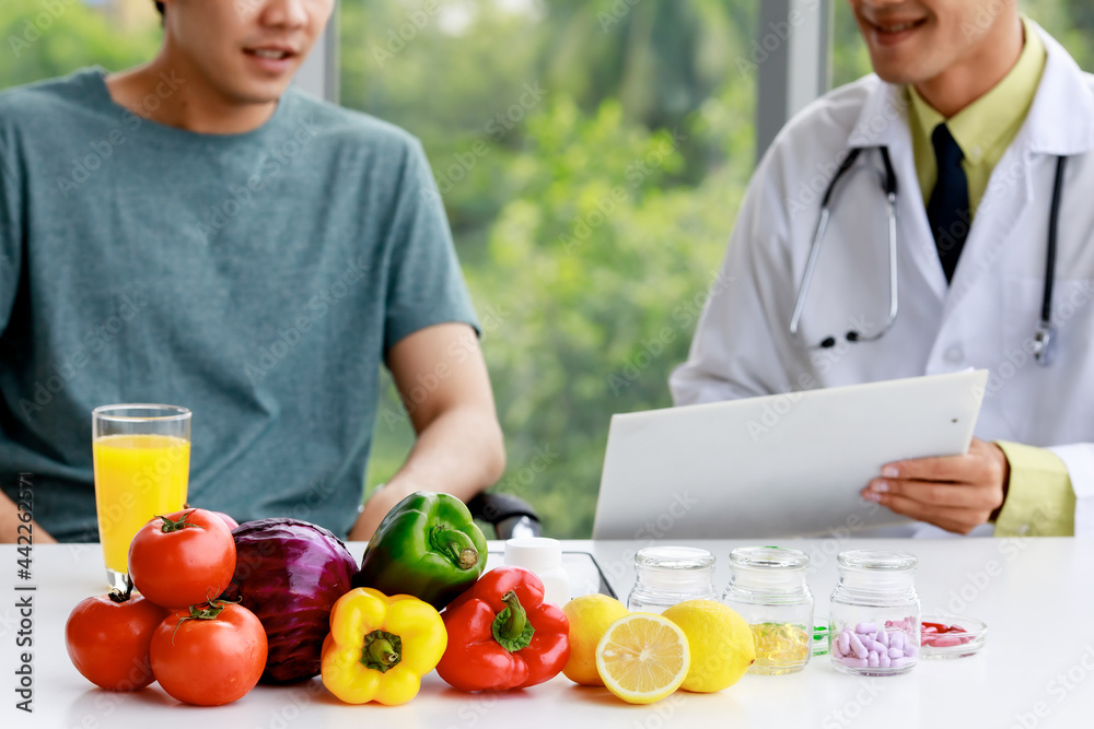 Asian nutritionist doctor wearing stethoscope holding documents and explaining it to patient. Fruits, juice and nutritions on the table Asian nutritionist doctor wearing stethoscope holding documents and explaining it to patient. Fruits, juice and nutritions on the table