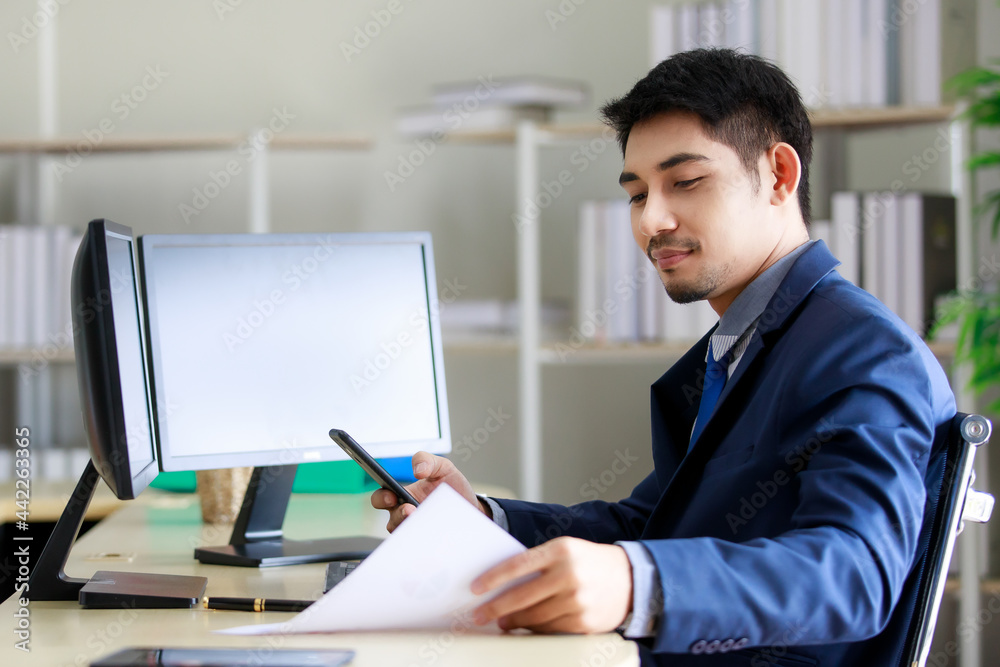 Confident and happy young Asian businessman working on company strategy in his private office. Business and success concept. Confident and happy young Asian businessman working on company strategy in his private office. Business and success concept.