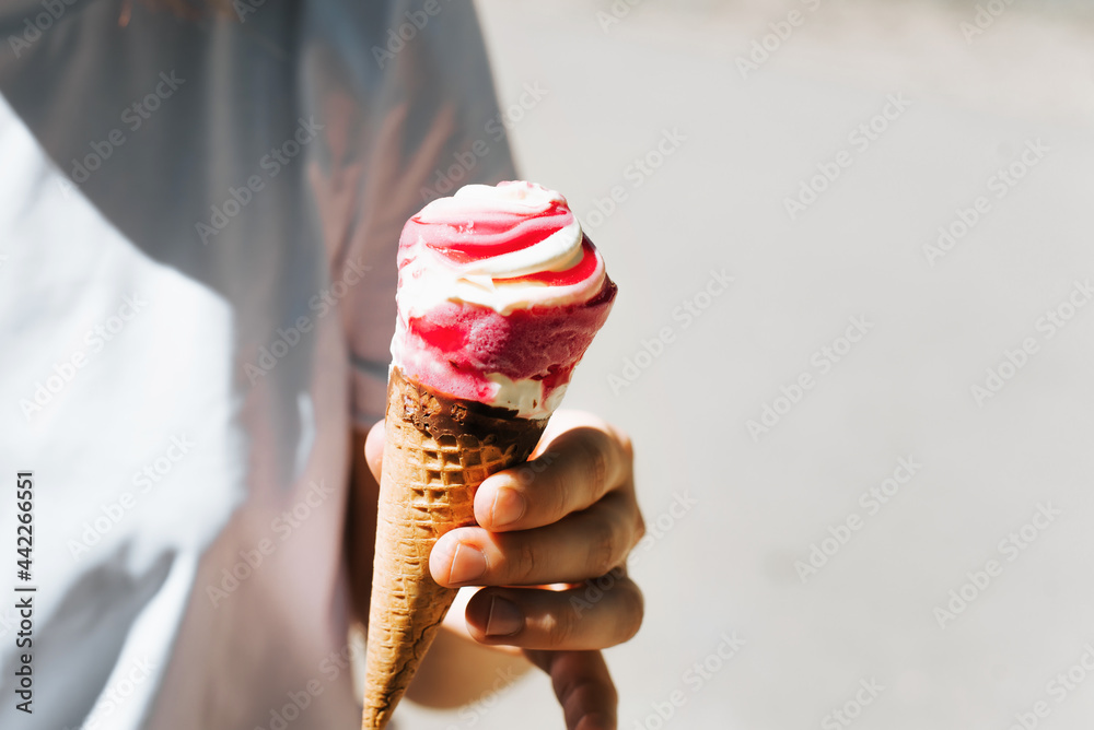 Close-up of a female hand holding an ice cream waffle cone, outdoors. Girl and red ice cream on a hot summer day, cropped image.