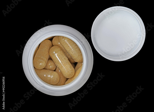 Close up top view of yellow capsules or pills in white bottle or plastic canister with cap on black background