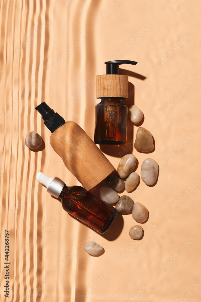 Bottles of cosmetic products and stones in water on color background