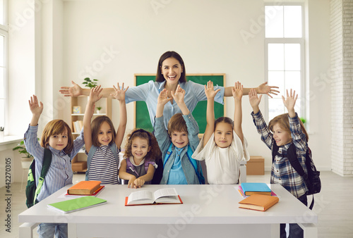 Murais de parede Happy teacher with arms widely spread to hug cheerful children raising hands