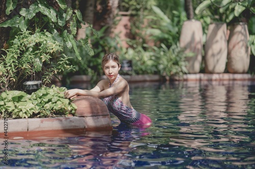 Woman in pink one piece swimsuit relax in tropical swimming pool, summer vacation.