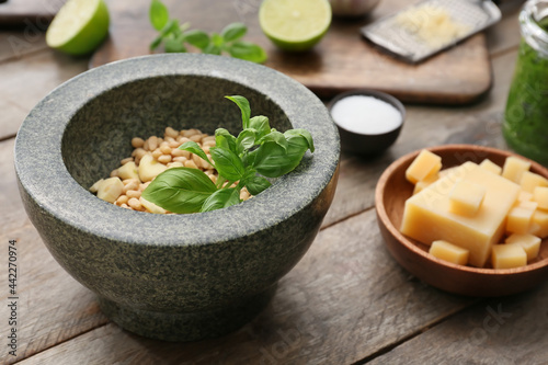 Mortar with basil leaves and cheese on wooden background