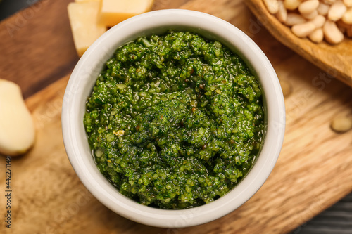 Board with bowl of fresh pesto sauce and ingredients on wooden table, closeup