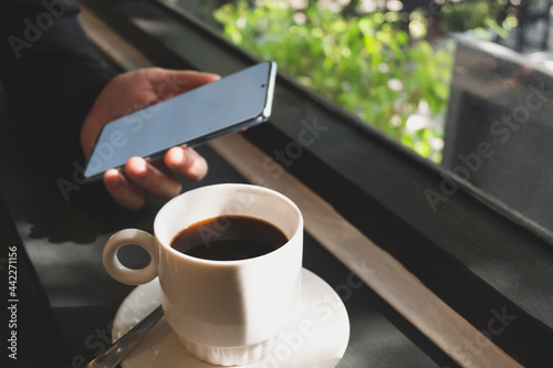 Close up image of a man holding mock up blank screen phone in a cafe with a coffee in front