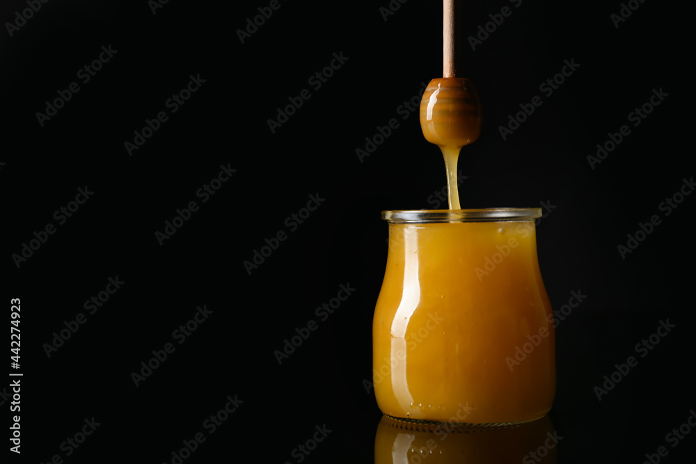 Honey pouring from dipper into glass jar on dark background Honey pouring from dipper into glass jar on dark background