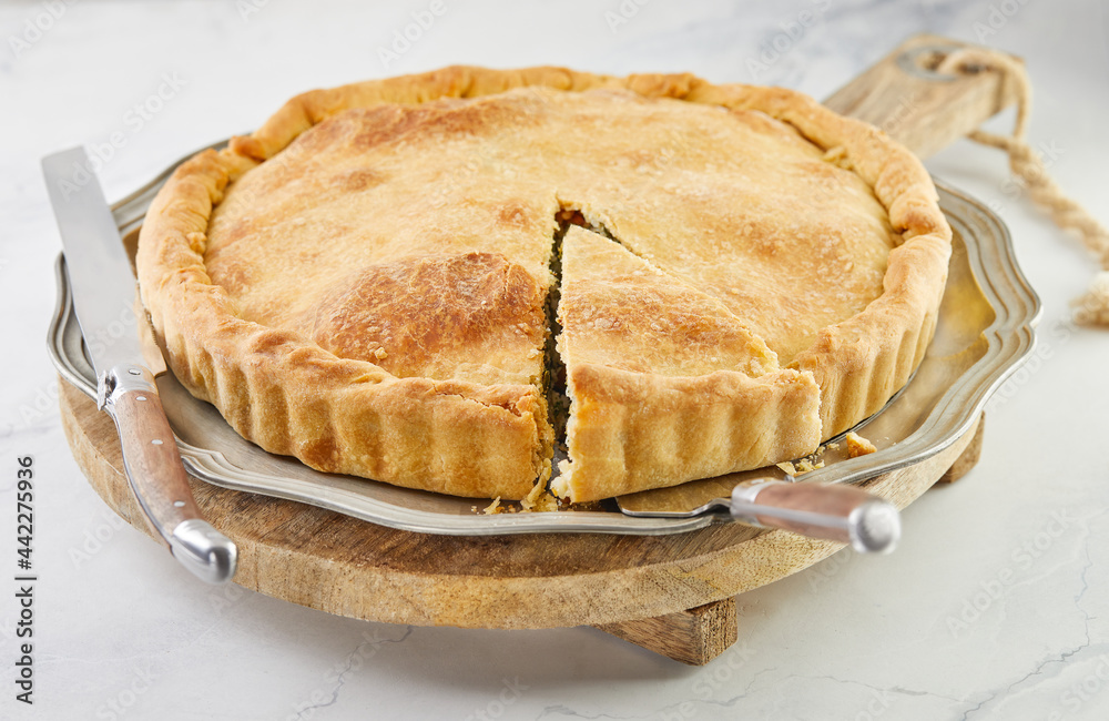 Ready Swiss pie with chard, rice, onions and pine nuts on a wooden stand on white marble