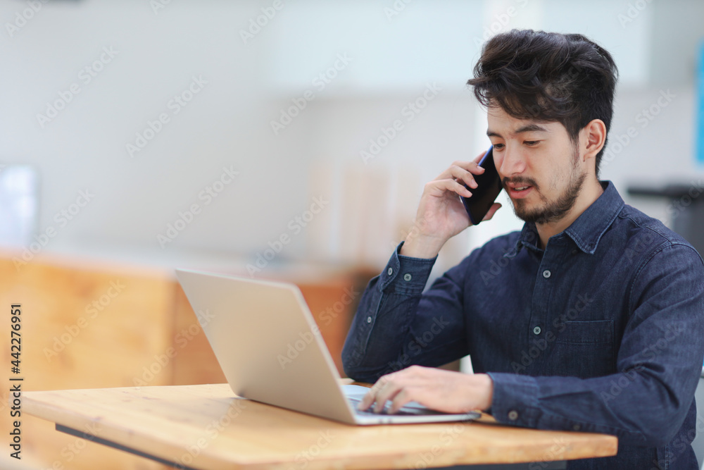 Young asian man talking on phone and working on laptop. Young asian man talking on phone and working on laptop.