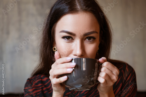 Portrait of a young woman of Caucasian appearance in a cafe with a cup of coffee. Beautiful brunette with brown eyes. Enjoying morning coffee in a cozy cafeteria