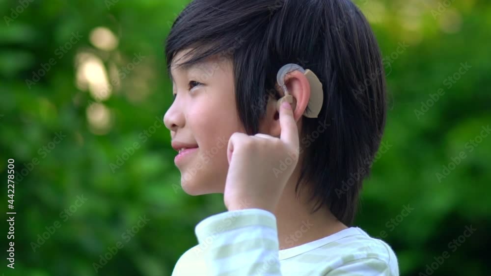 Asian Child With Hearing Aid Behind The Ear Outdoors Asian Child With Hearing Aid Behind The Ear Outdoors