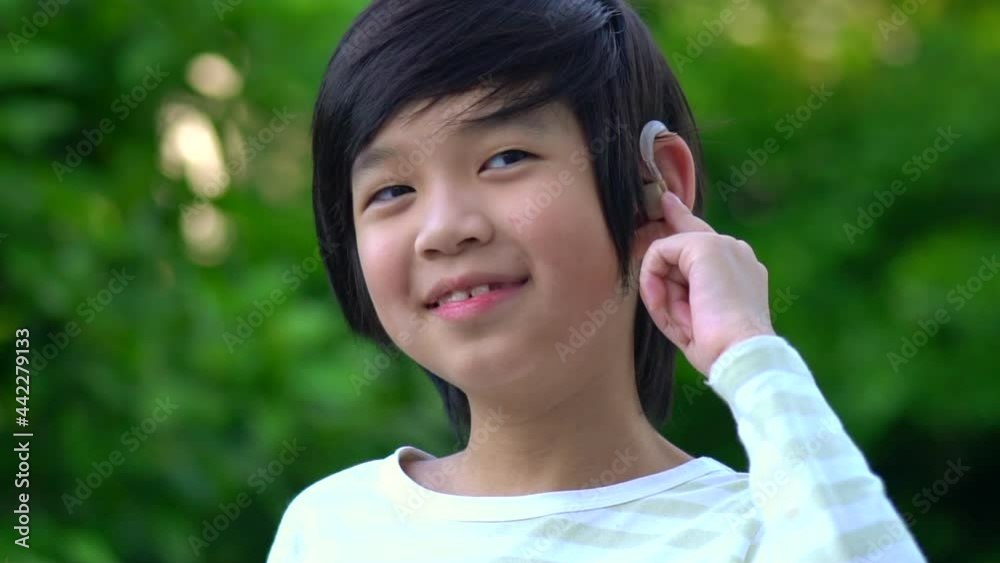 Asian Child With Hearing Aid Behind The Ear Outdoors Asian Child With Hearing Aid Behind The Ear Outdoors