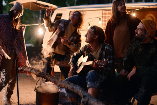 Happy young friends dancing and singing songs with guitar during camping in the forest