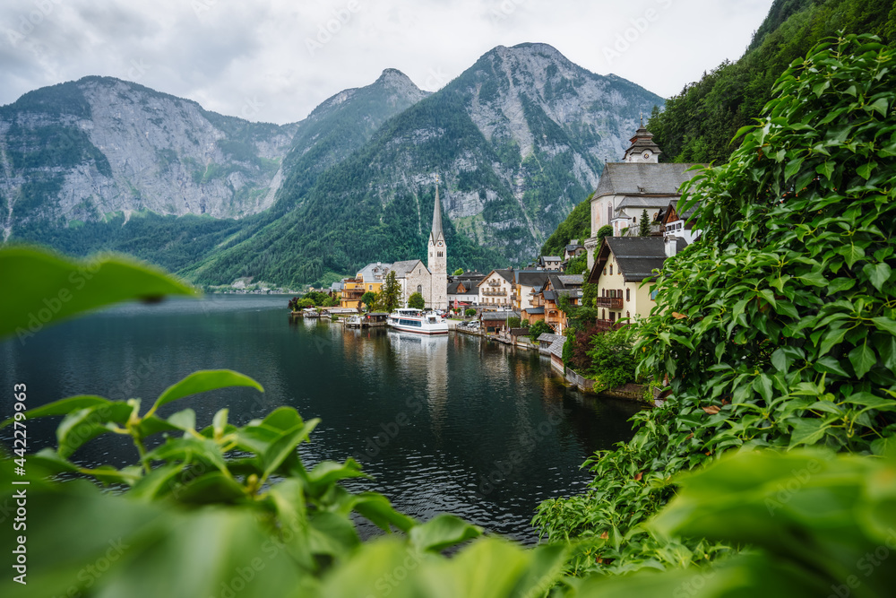 Famous lake side view of Hallstatt village with Alps behind, Foliage leaves framed. Austria