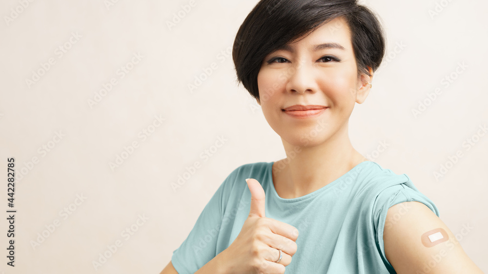 COVID-19 vaccination concept. Beautiful middle-aged Asian woman smiling and thumbs up, show band aid on arm after vaccine injection and no side effect. Herd Immunity, Vaccinated, Hospital, Insurance COVID-19 vaccination concept. Beautiful middle-aged Asian woman smiling and thumbs up, show band aid on arm after vaccine injection and no side effect. Herd Immunity, Vaccinated, Hospital, Insurance