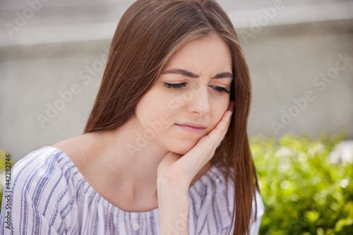 Portrait Of Worried Young Woman Suffering With Depression With Head In Hands Outdoors