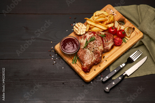 Grilled roated beef steaks, potato and sauce on wooden cutting board photo