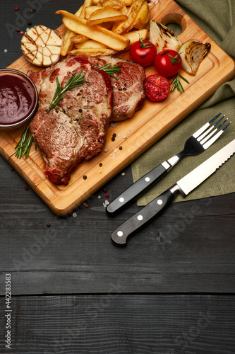 Grilled roated beef steaks, potato and sauce on wooden cutting board