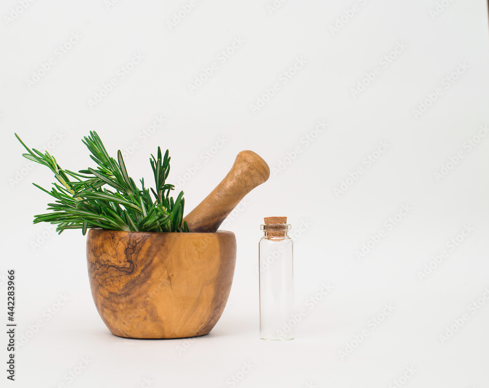 Rosemary in wooden mortar  pestle and empty glass bottle on white background.