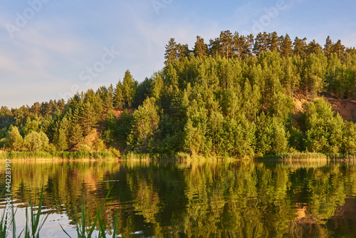  Hills covered with forest are reflected in the surface of the lake.